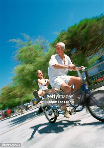 senior man and young girl riding bikes, blurred motion - mitziehen stock-fotos und bilder