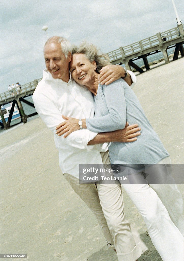 Couple embracing on the beach, smiling at camera.