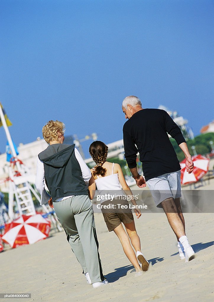 Senior couple walking with young girl on the beach, rear view.