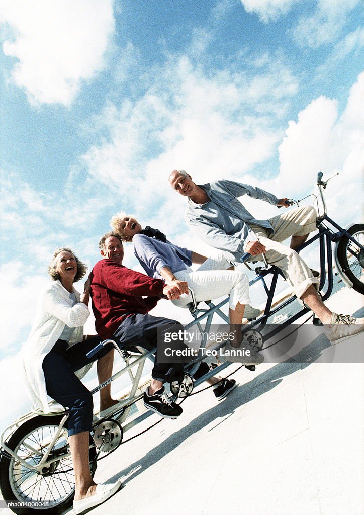 Senior couples on tandem bike at beach, portrait.