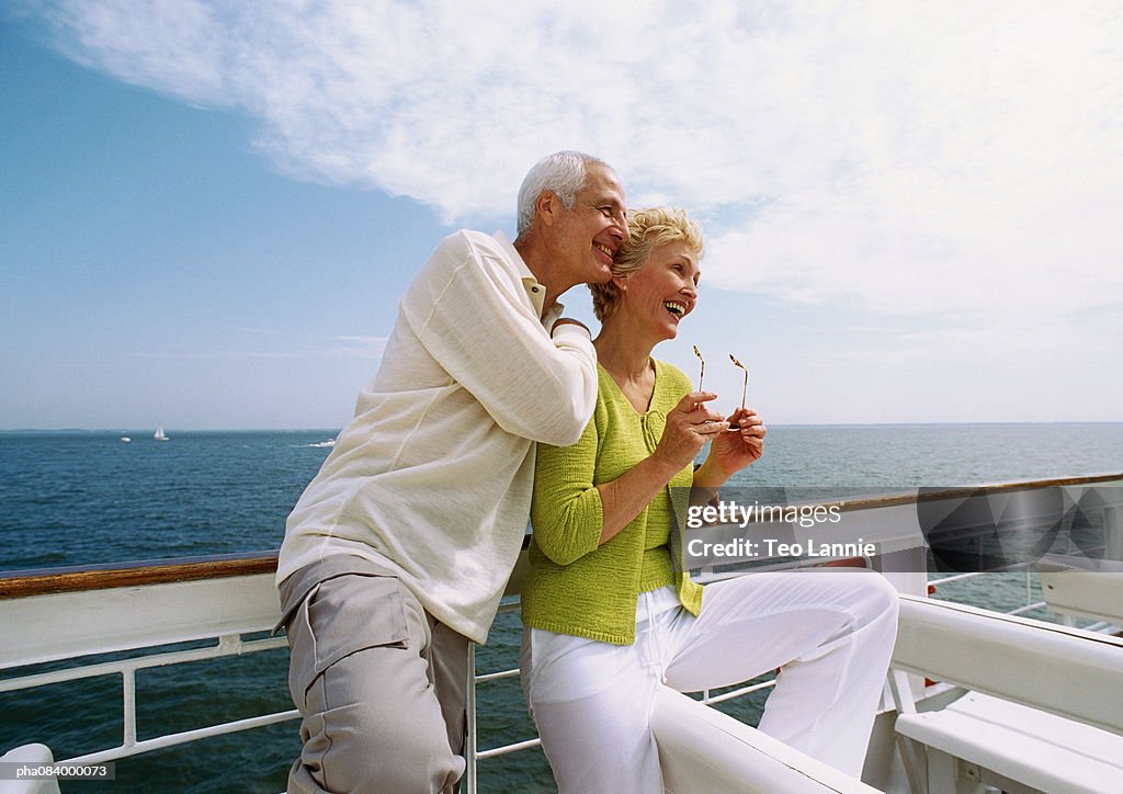 Senior couple leaning on railing, smiling.