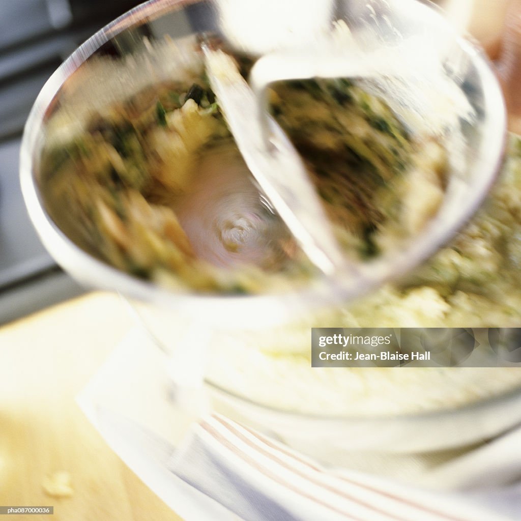 Close-up of food being mixed in bowl, blurry.