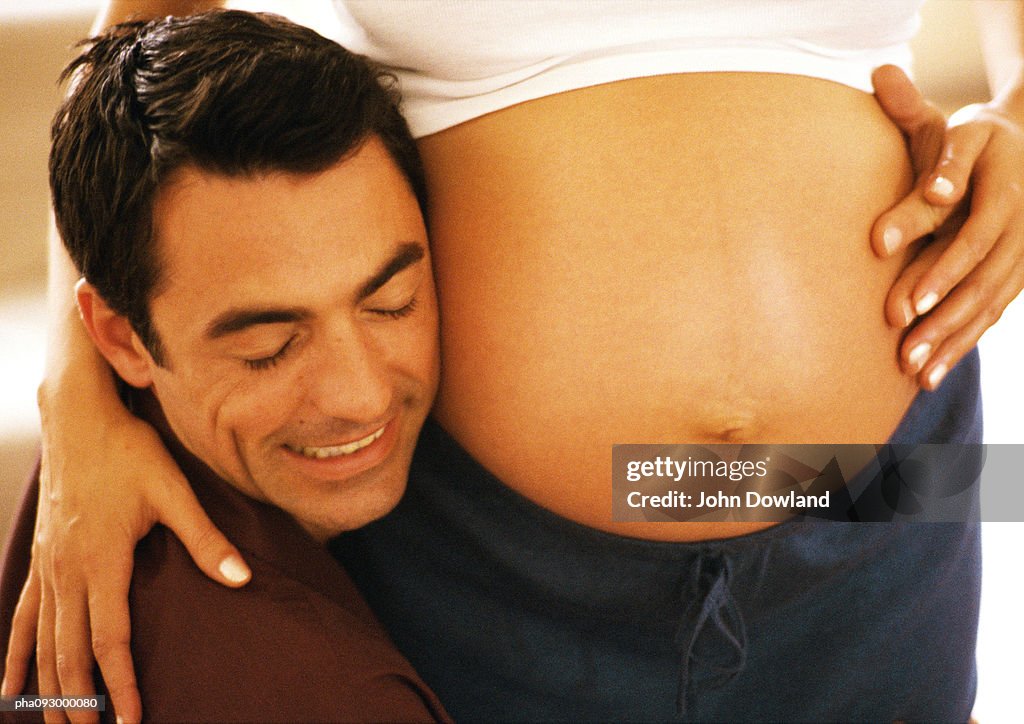 Man pressing head to pregnant woman's stomach, close-up
