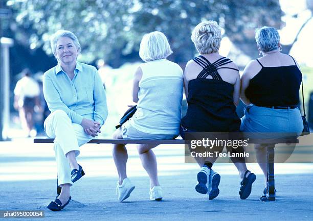 four mature women sitting on a bench, three seen from the back - being watched stockfoto's en -beelden