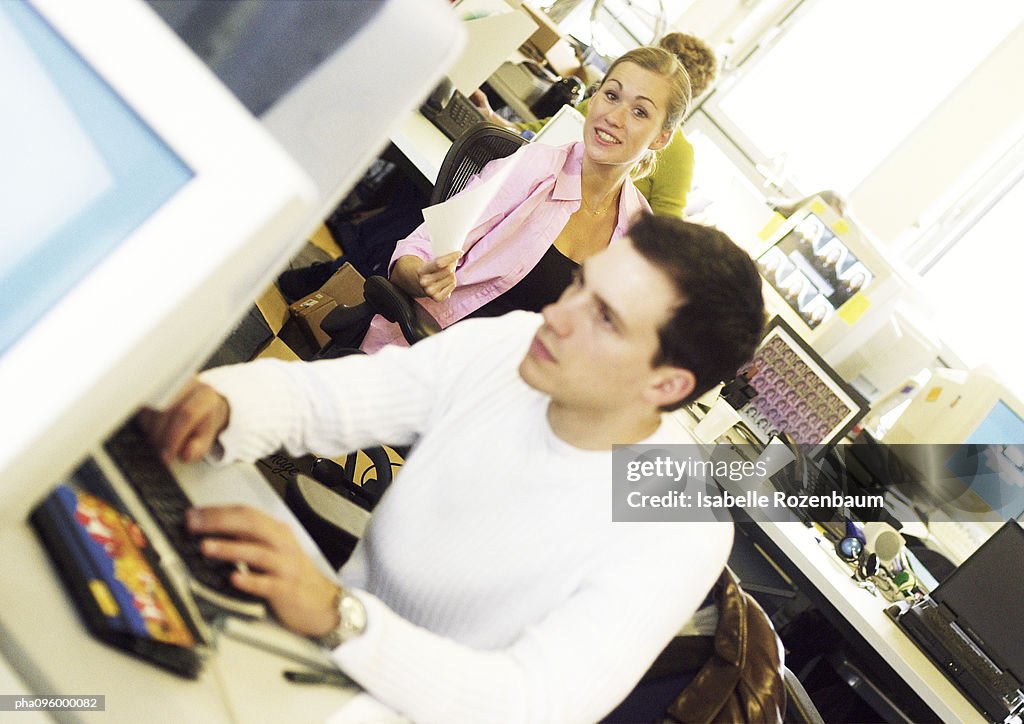Woman smiling, man working on computer