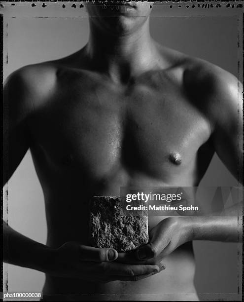 torso of nude man holding stone cube on palm of hands in front of stomach, partial view, mid section, b&w - brustmuskulatur stock-fotos und bilder