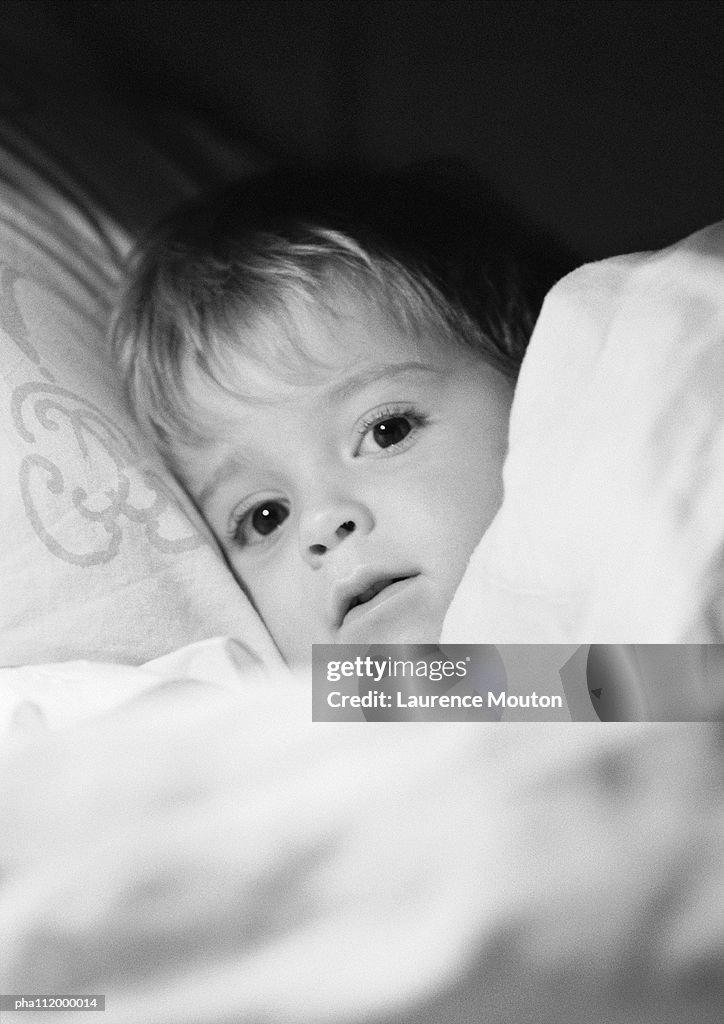 Small boy in bed under blanket, close-up, b&w