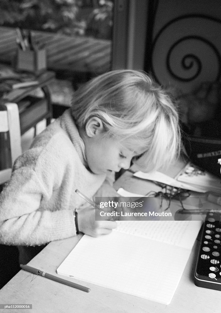 Girl sitting at desk, writing in notebook, b&w