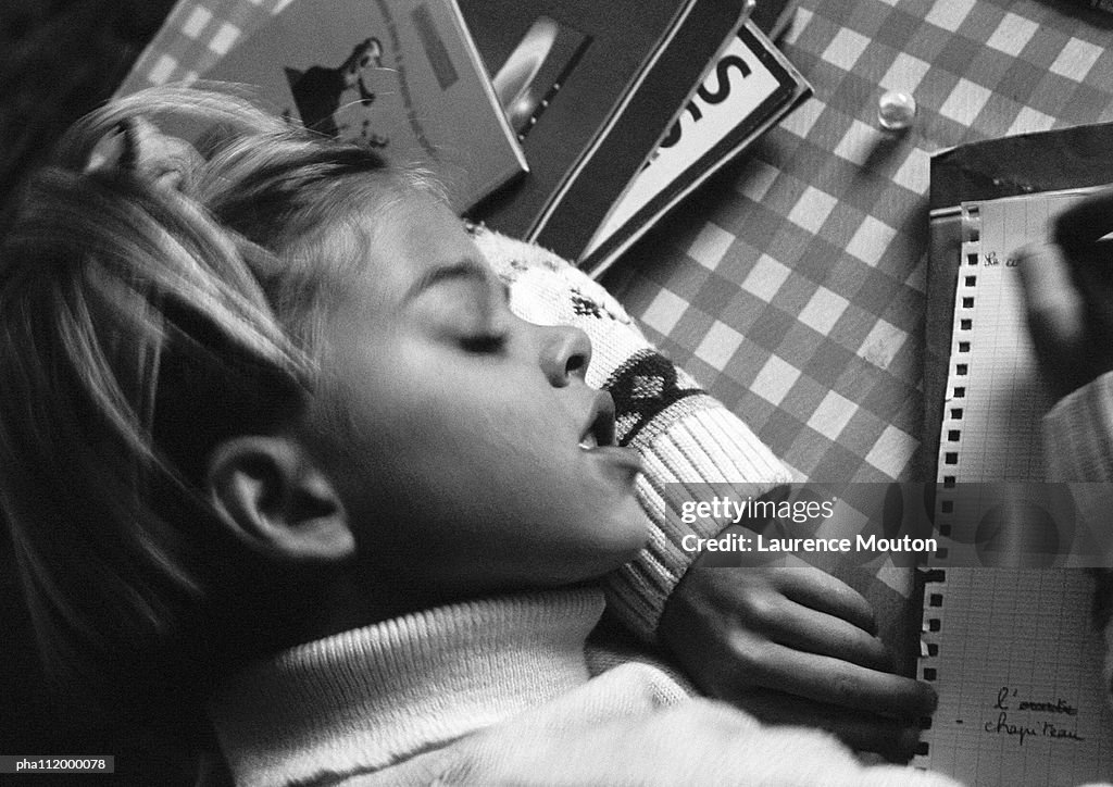 Girl resting head on arm writing, elevated view, b&w