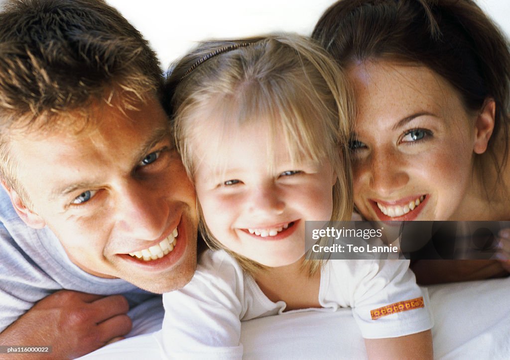 Small girl laying between parents, smiling, close-up