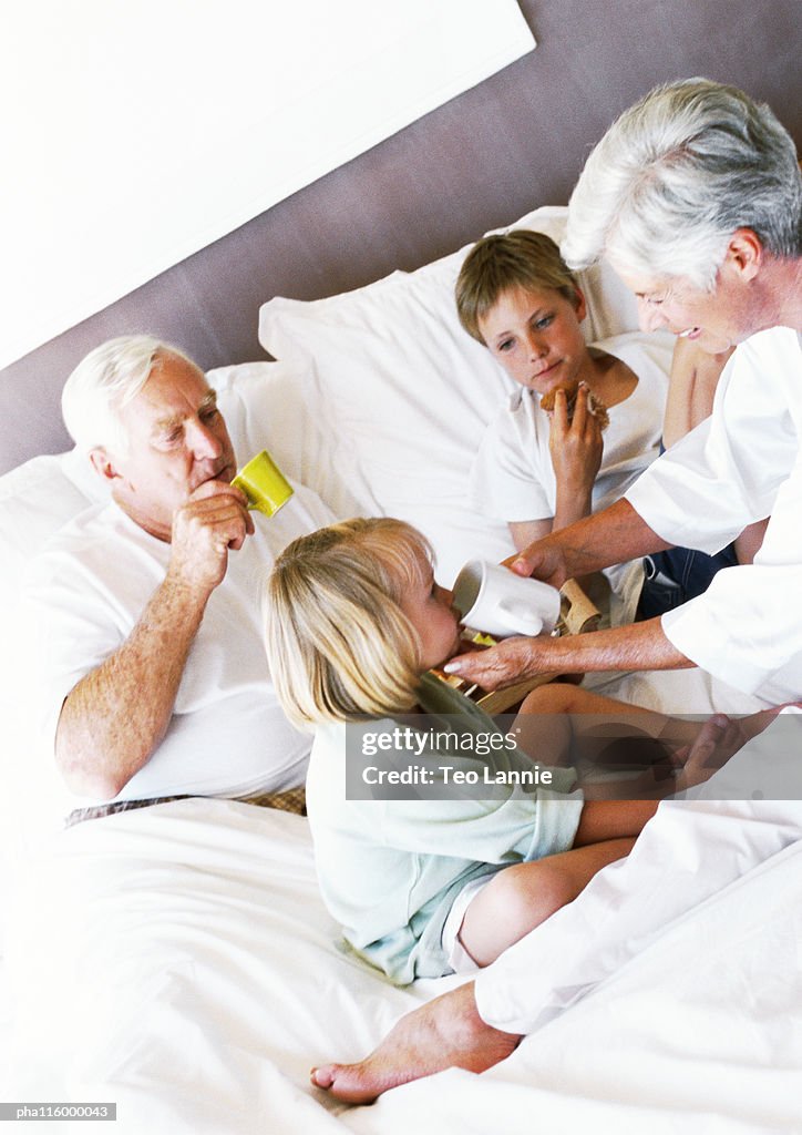 Grandparents and children on bed, drinking