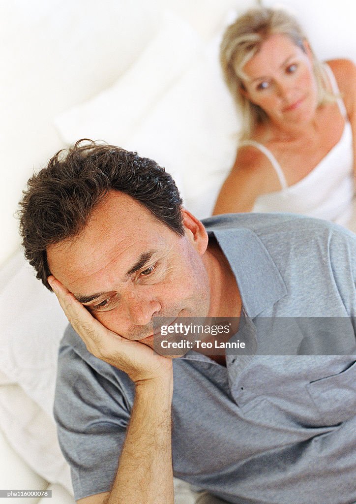Woman sitting in bed behind man with hand on cheek