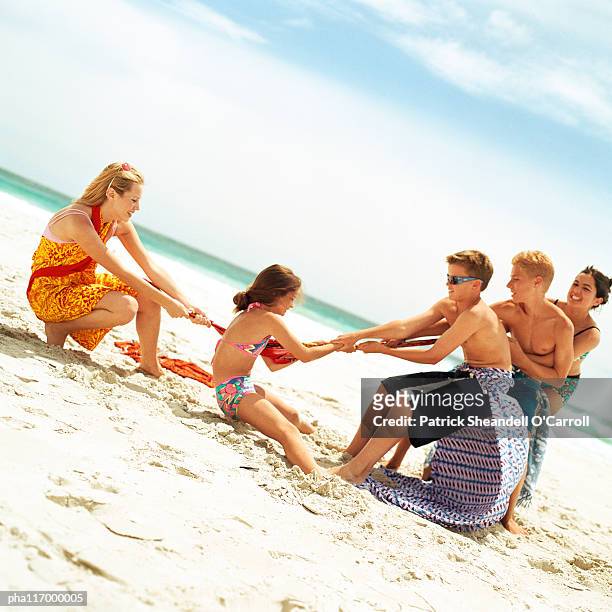 group of people playing tug of war at the beach - war stock-fotos und bilder