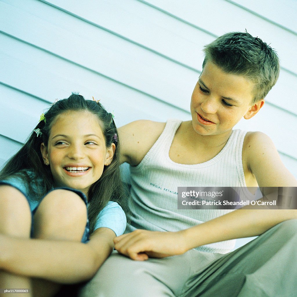 Two teenagers sitting side by side, outside