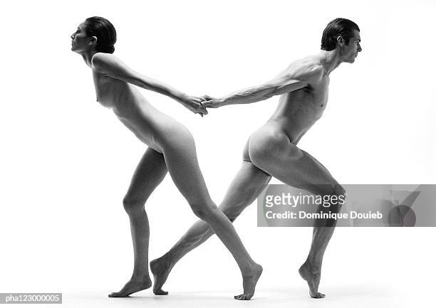 nude man and nude woman leaning away from each other, holding hands from behind, b&w - man and woman holding hands profile stockfoto's en -beelden
