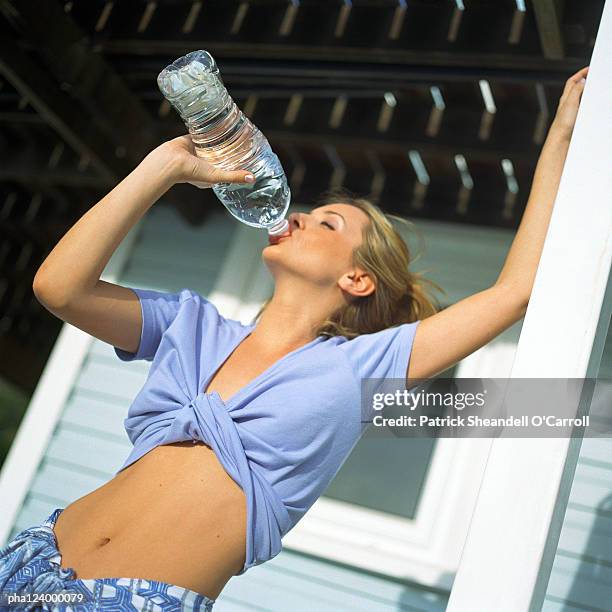 woman drinking from plastic bottle, low angle view - female navel ストックフォトと画像