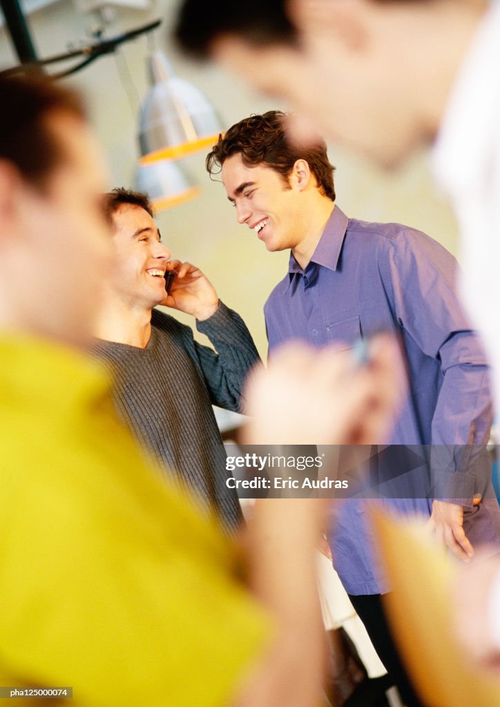 Two men talking, one using cell phone