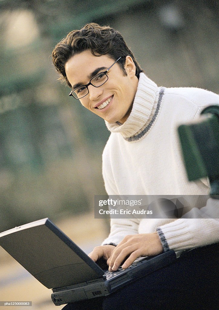 Man sitting on bench with laptop computer, portrait