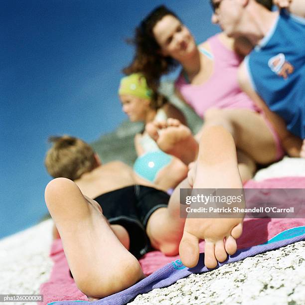 couple and children lying on beach, focus on child's feet - woman lying on stomach with feet up stock pictures, royalty-free photos & images