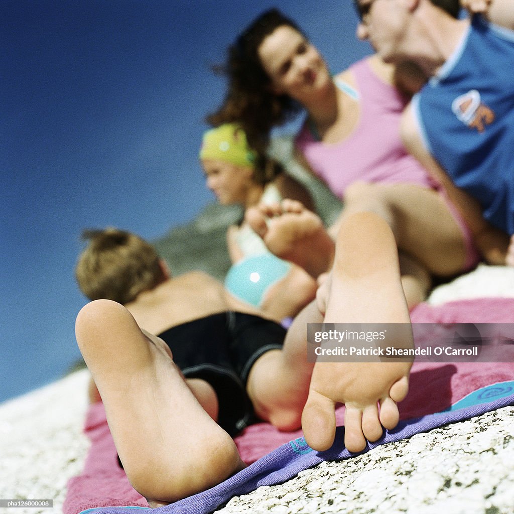 Couple and children lying on beach, focus on child's feet