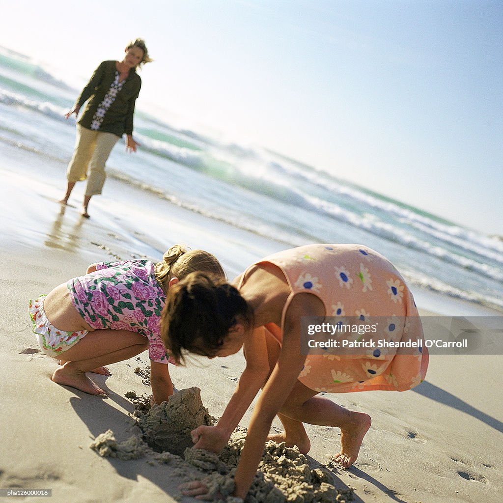 Woman walking on beach, children digging in sand