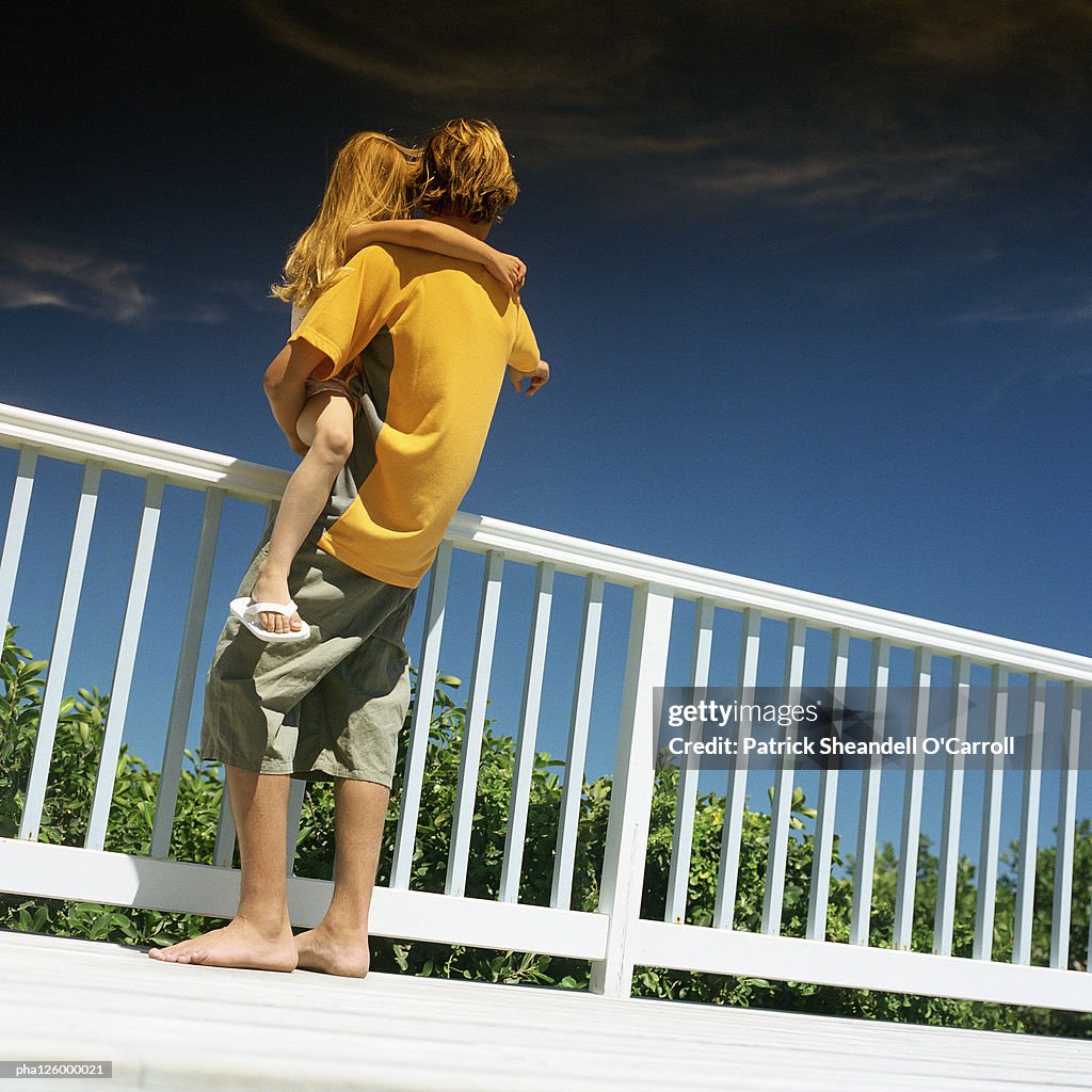 Teenage boy carrying girl, outside, rear view