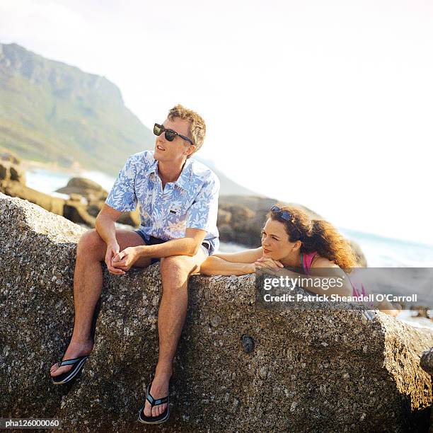 mature couple resting on rock, sea in background - being watched stockfoto's en -beelden