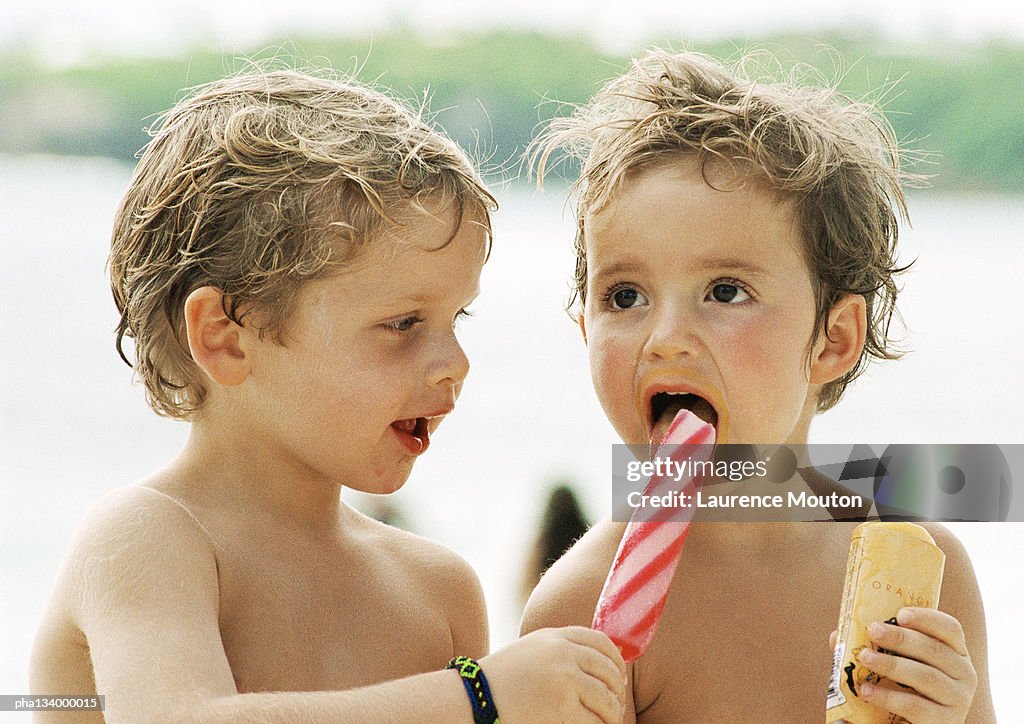 Two small children sharing popsicles, head and shoulders, portrait.