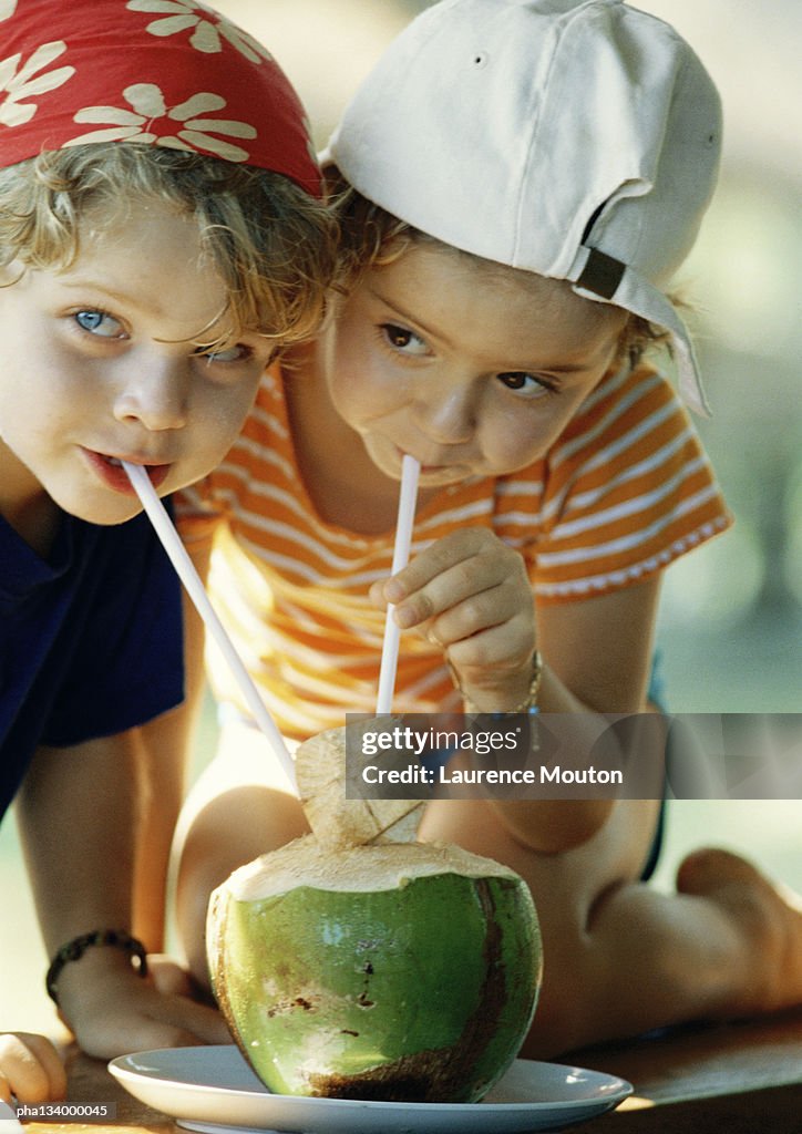 Two children drinking fresh juice through straws, close-up