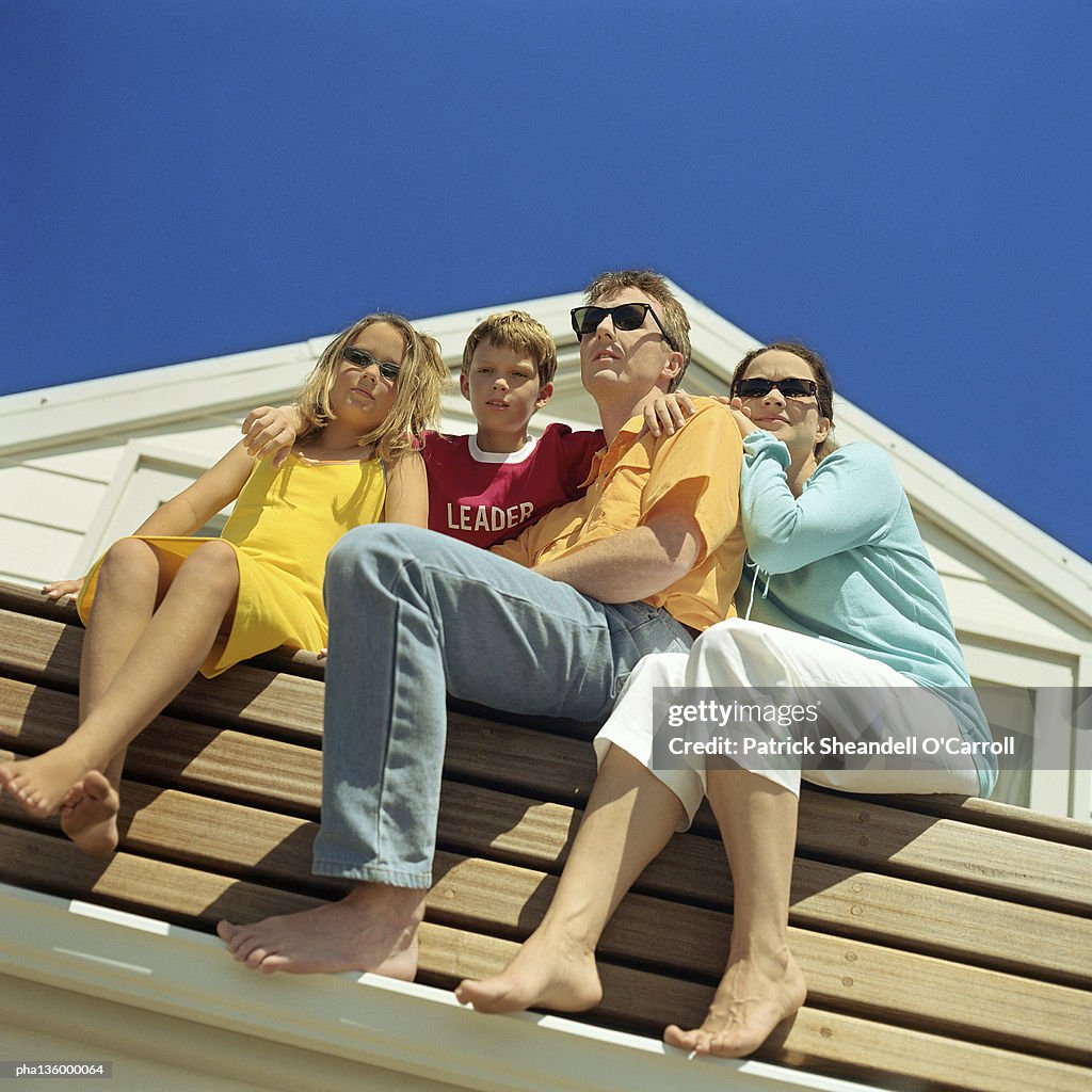 Upward angled shot of family sitting on bench, all wearing sunglasses