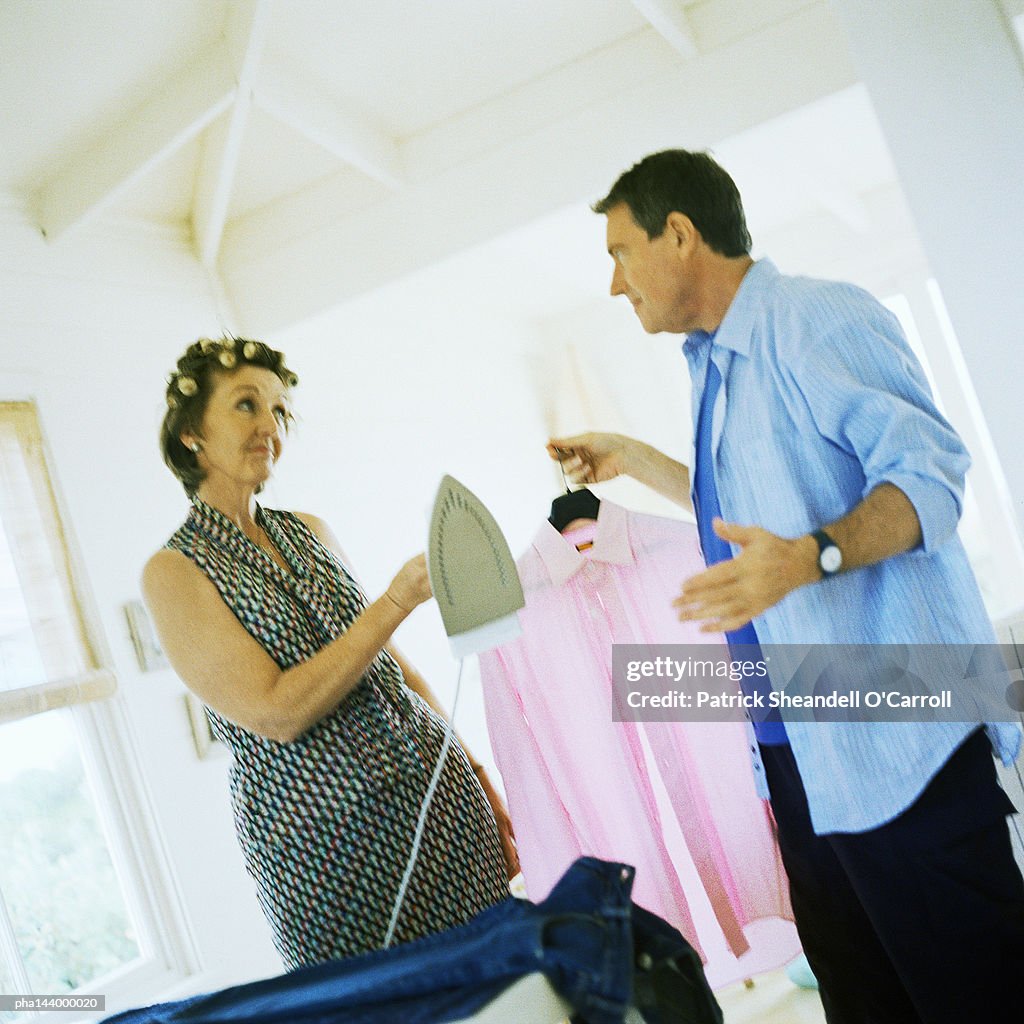 Mature woman holding iron, man holding shirt