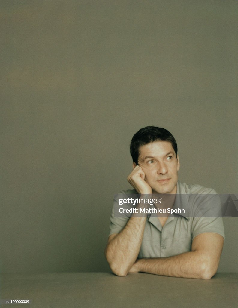 Man with elbows on table, resting head on right hand, portrait