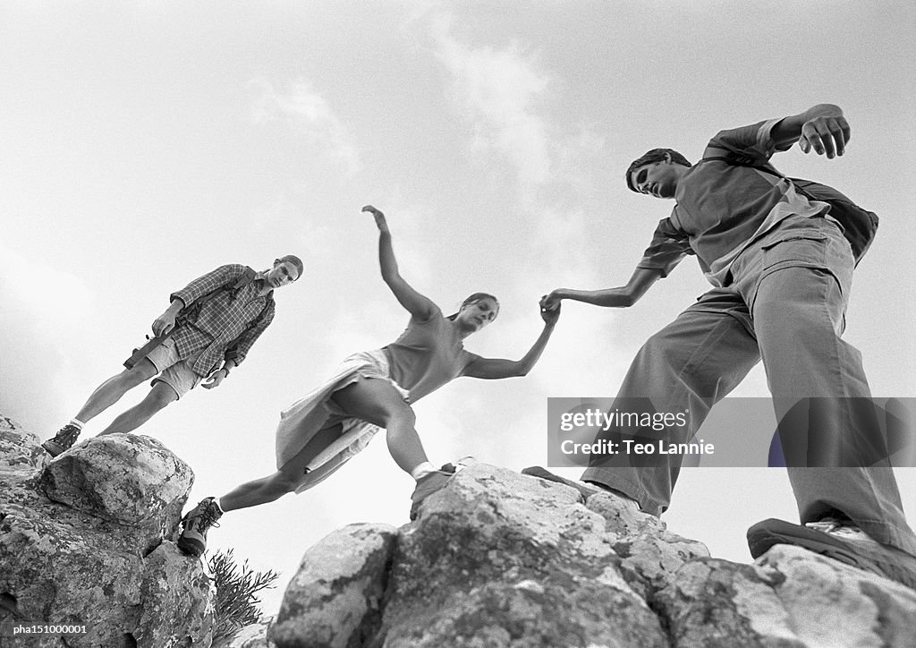 Three young people climbing on rocks, woman being aided, low angle view, b&w.