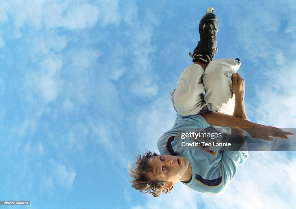 Young man on rollerblades, jumping, mid-air, low angle.