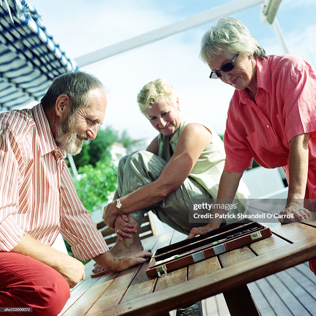 Three mature adults playing backgammon.