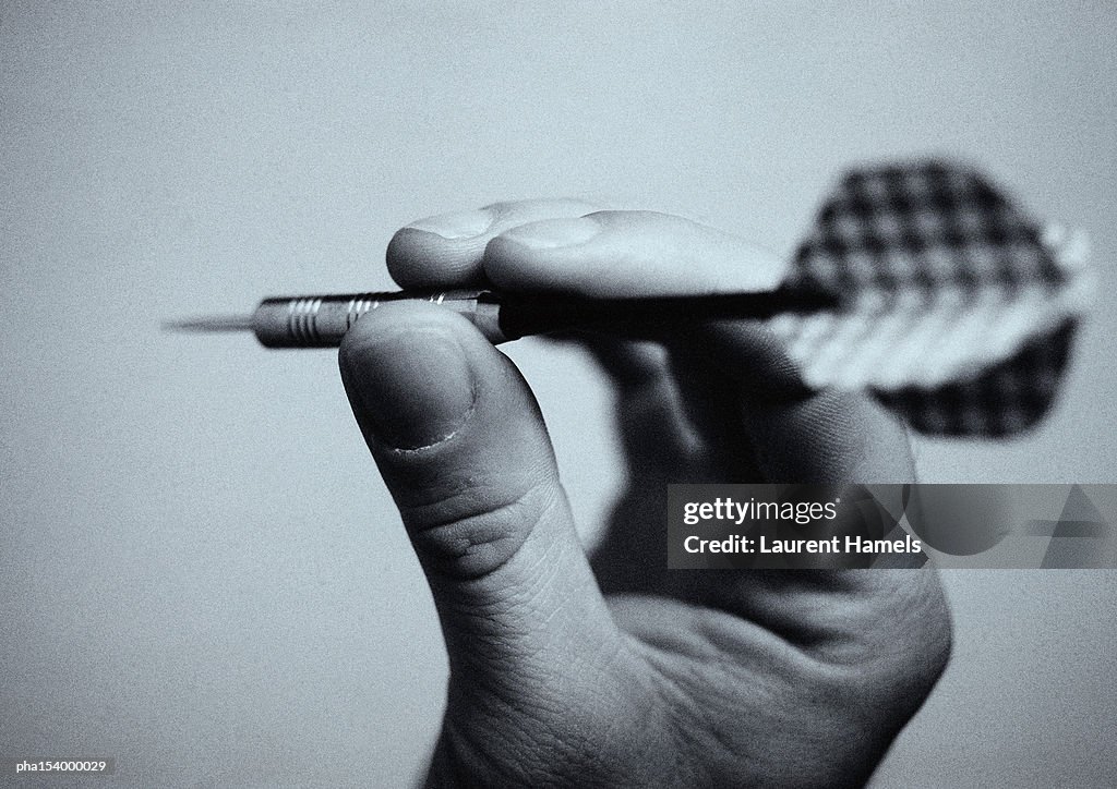 Hand holding dart, close-up, b&w.