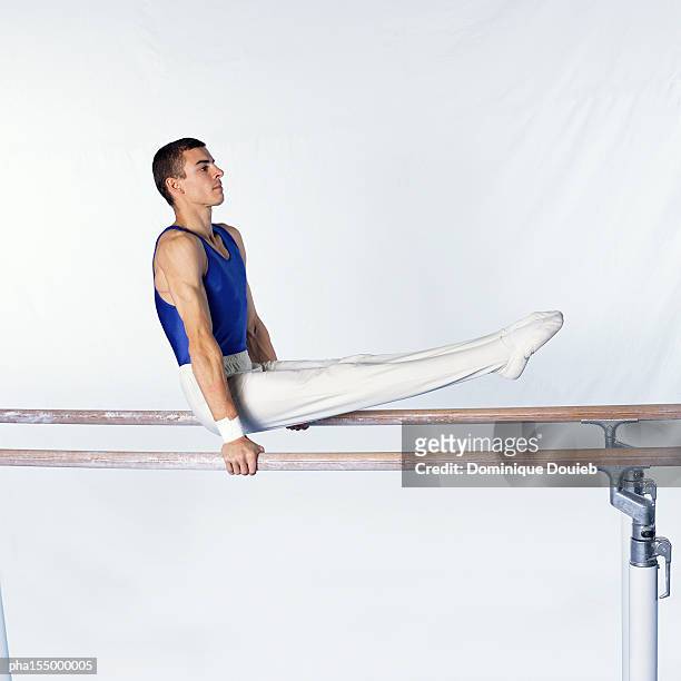 young male gymnast on parallel bars, side view. - parallel bars stockfoto's en -beelden