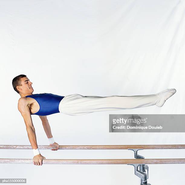 young male gymnast performing routine on parallel bars, side view. - parallel bars stockfoto's en -beelden