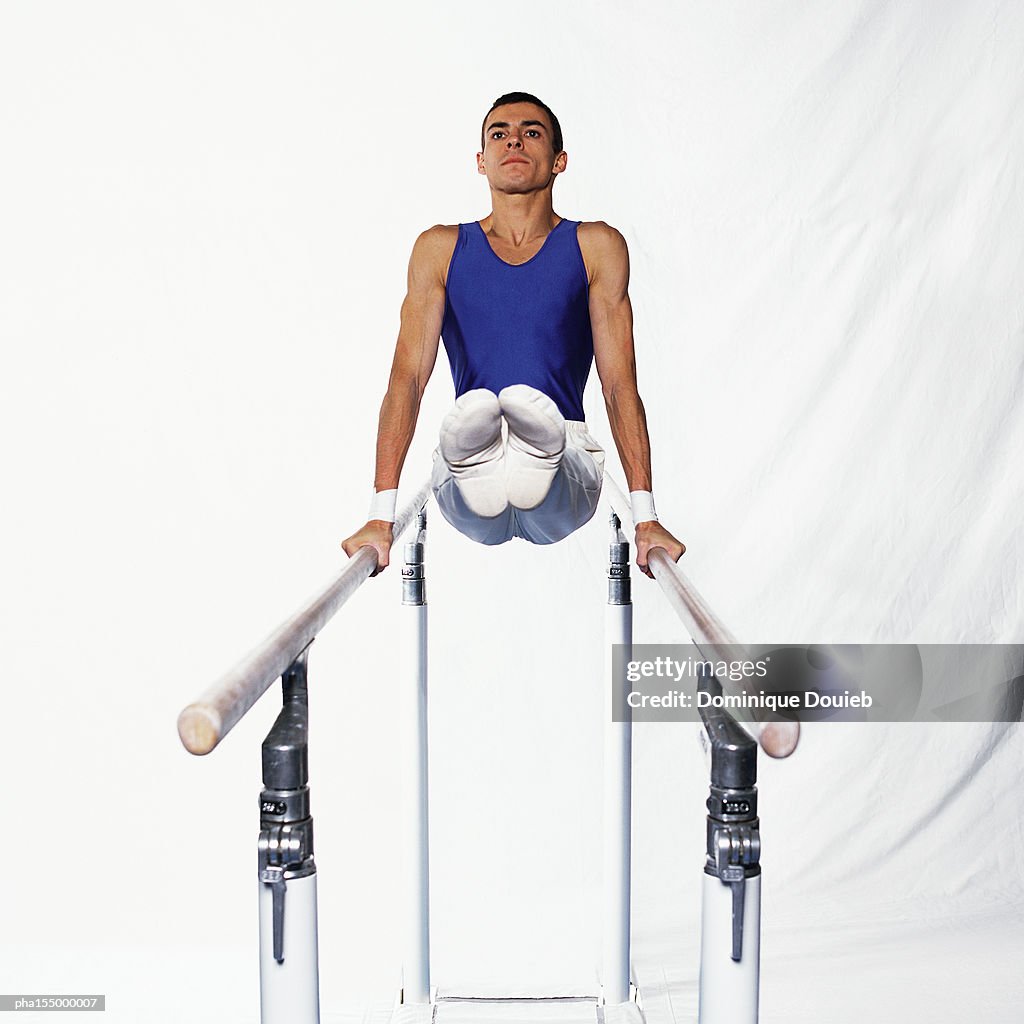 Young male gymnast on parallel bars, side view.