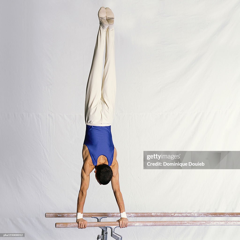 Young male gymnast performing routine on parallel bars, rear view.