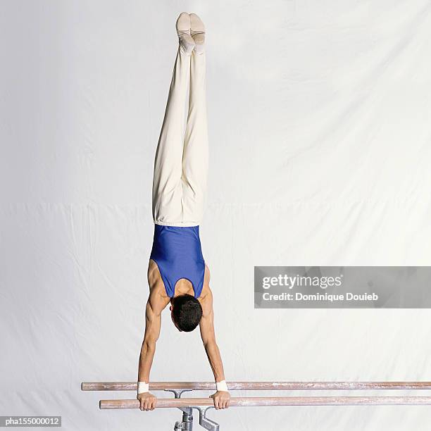 young male gymnast performing routine on parallel bars, rear view. - parallel bars stockfoto's en -beelden