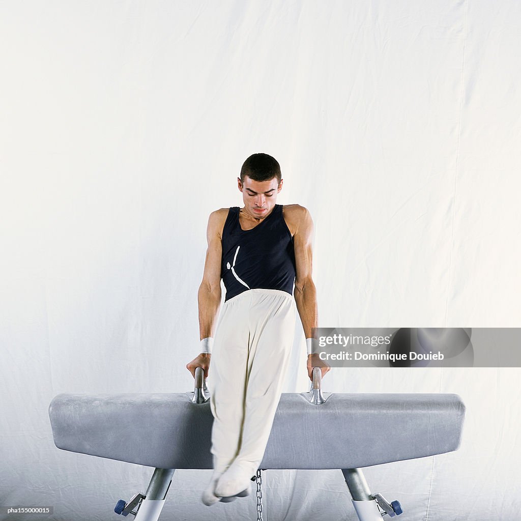 Young male gymnast performing routine on pommel horse.