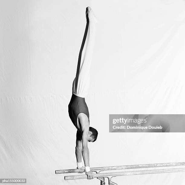 young male gymnast upside down on parallel bars, side view. - parallel bars gymnastics equipment photos et images de collection