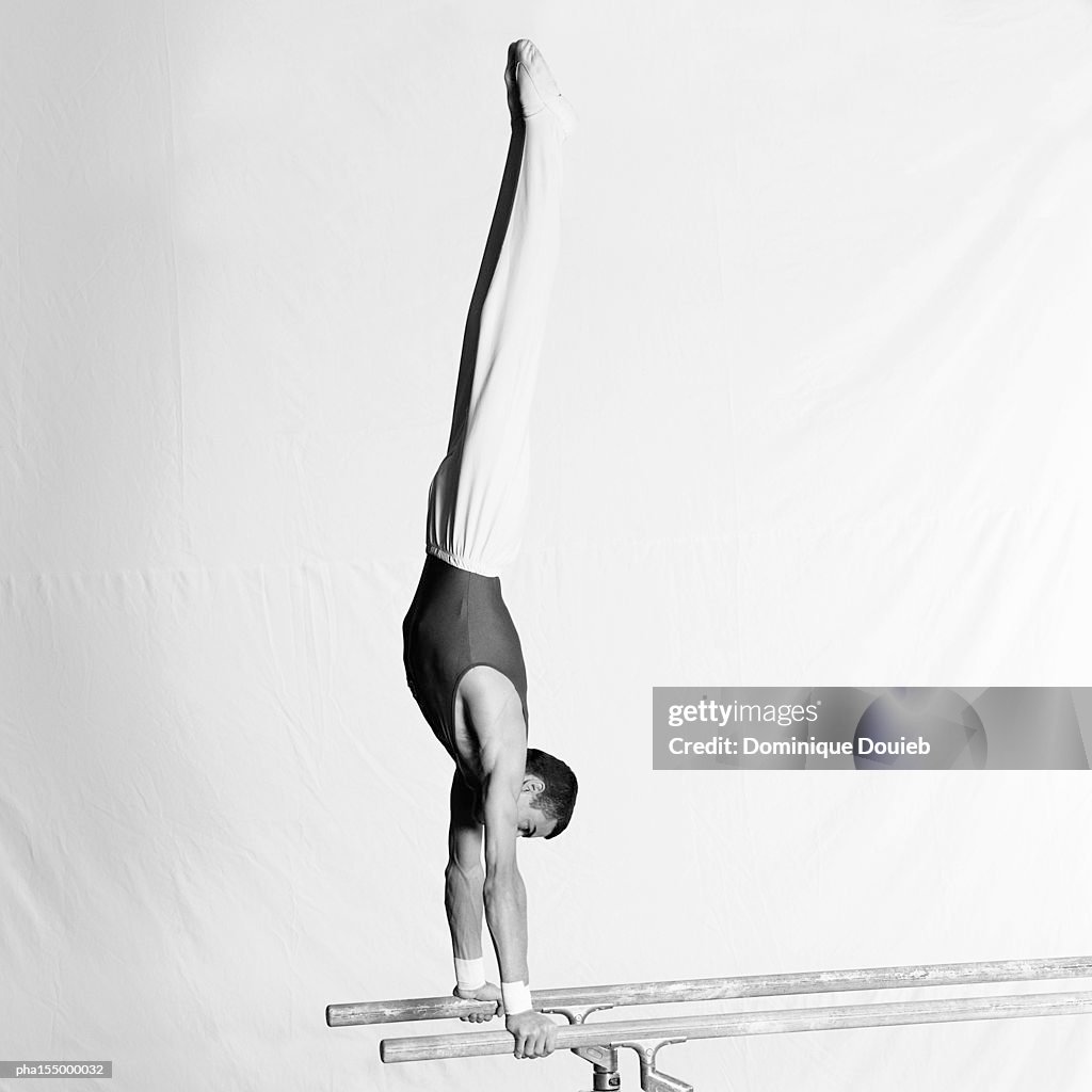 Young male gymnast upside down on parallel bars, side view.