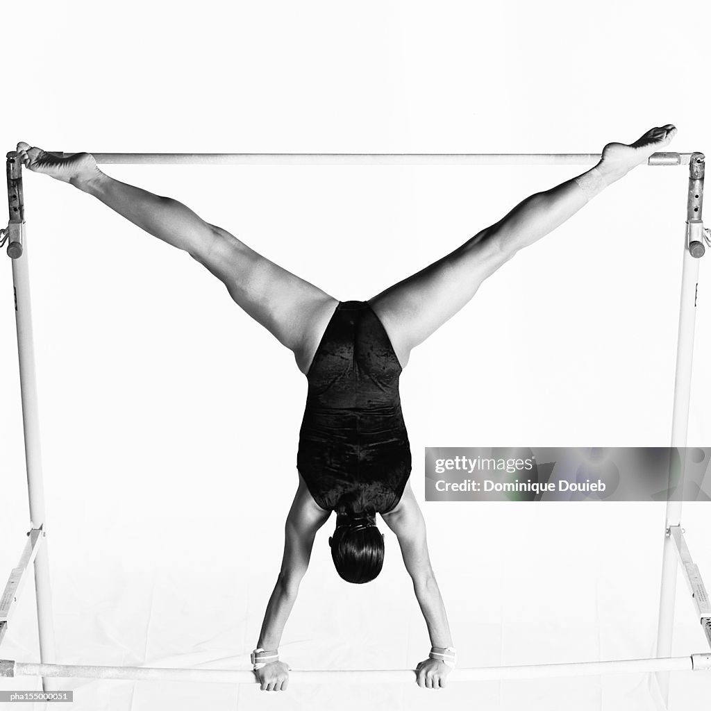 Young female upside down on uneven bars, rear view, b&w.