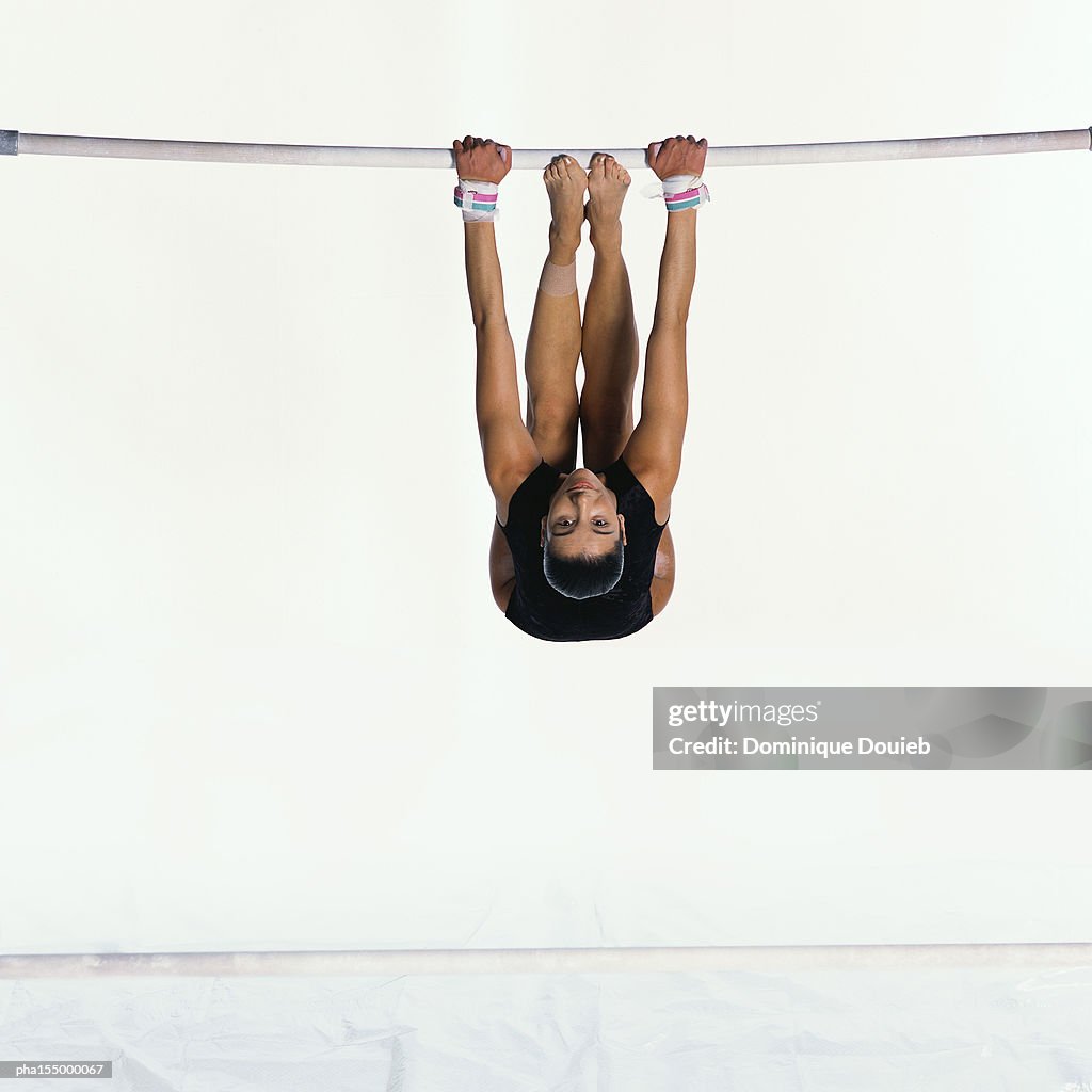 Young female gymnast upside down on uneven bars, looking into camera.