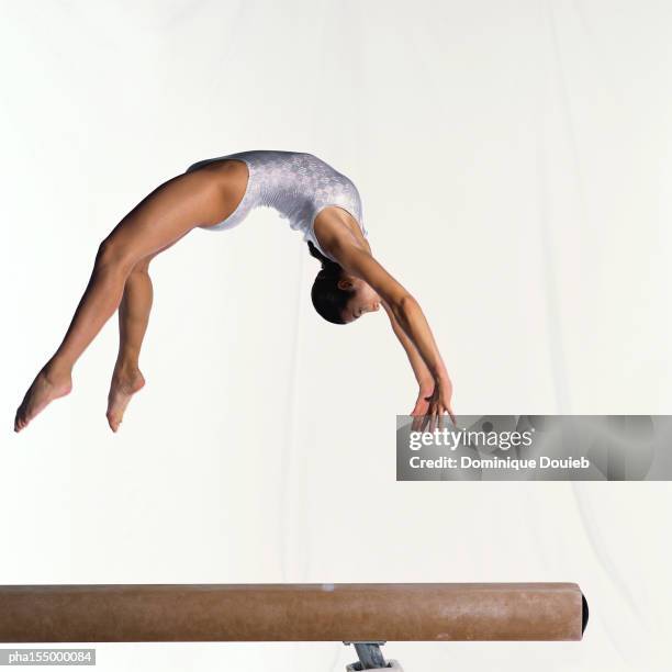 young female gymnast on balance beam performing exercise, mid-flight, side view. - turngerät stock-fotos und bilder