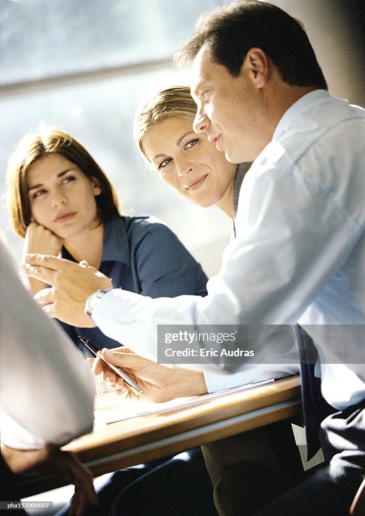 Man sitting at table speaking , two women looking at him