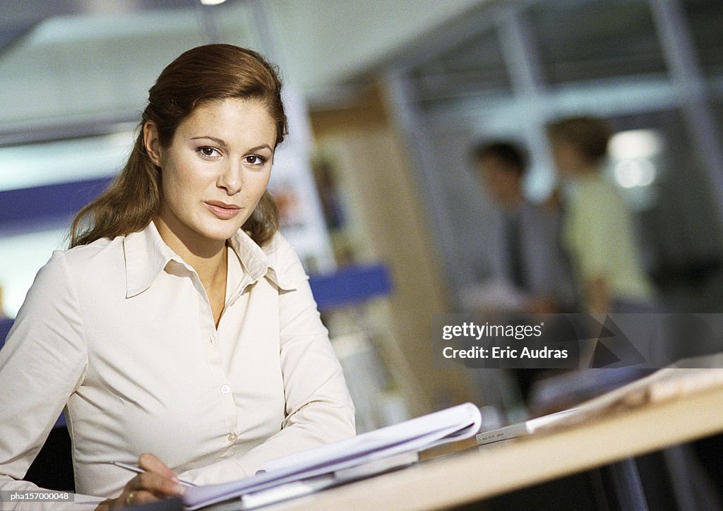 Young woman looking into camera, head and shoulders, office setting in background