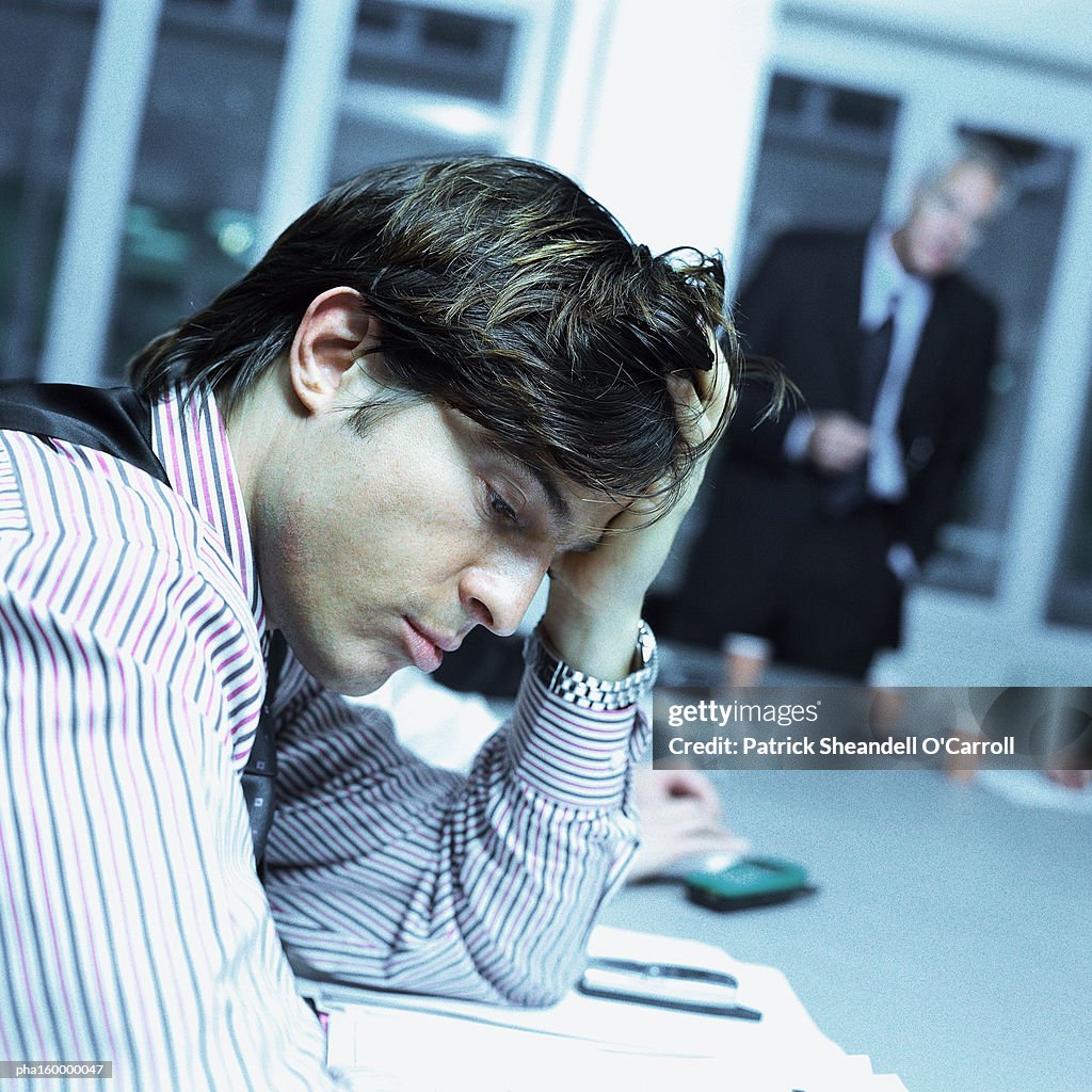 Young businessman sitting at desk looking down, side view.